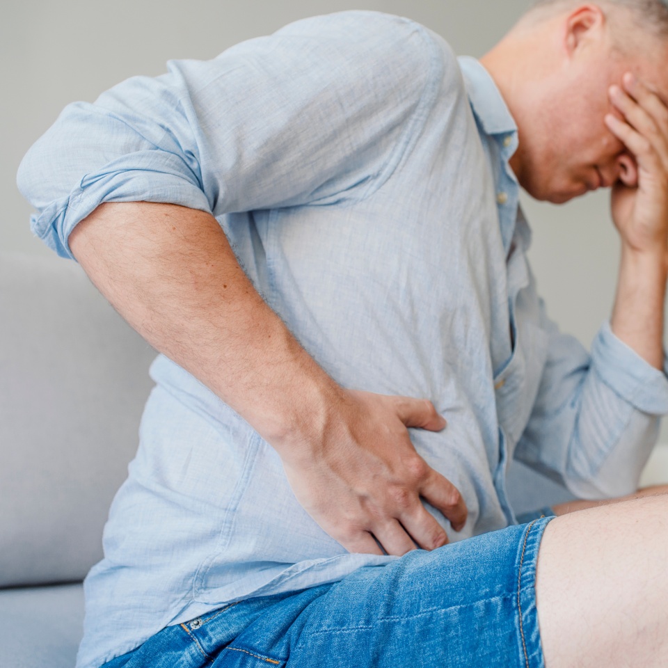 Terrible stomachache. Frustrated handsome young man hugging his belly and keeping eyes closed. Disturbed male having pain in stomach