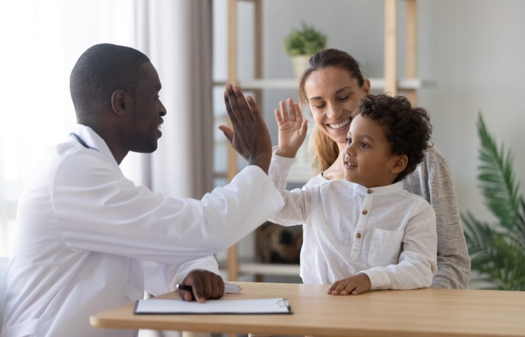 Happy cute multiracial child boy give high five to african man pediatrician welcome little patient and mom at consultation trusting kid with doctor celebrate good medical health care treatment result