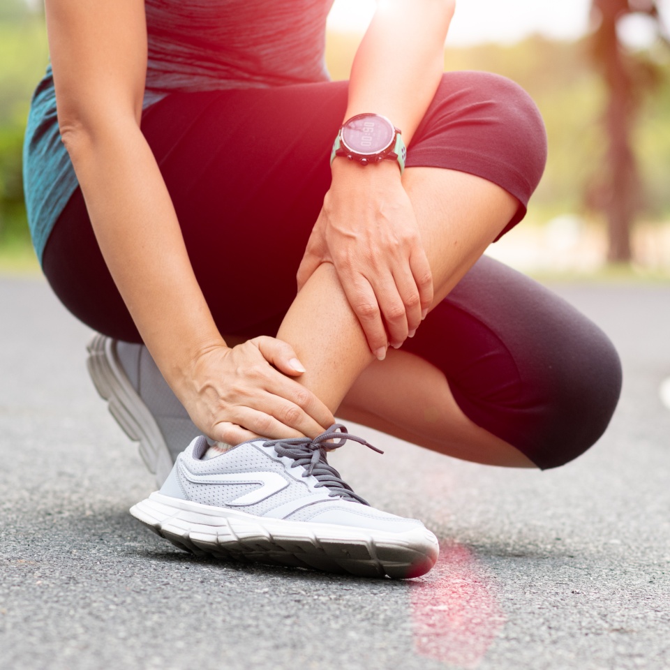 Young woman suffering from pain in leg during running outdoor. Healthcare concept.