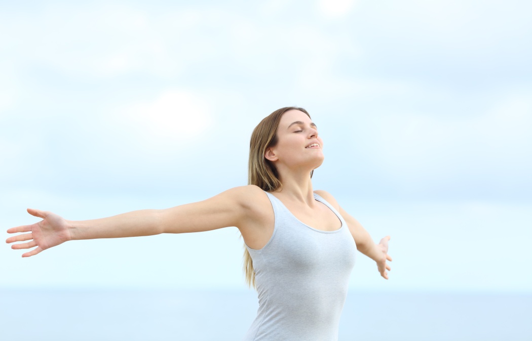 Happy woman breathing deeply fresh air outstretching arms on the beach