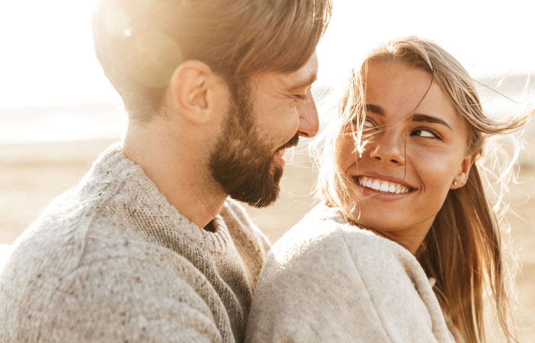 Close up of a smiling beautiful young couple embracing while standing at the beach
