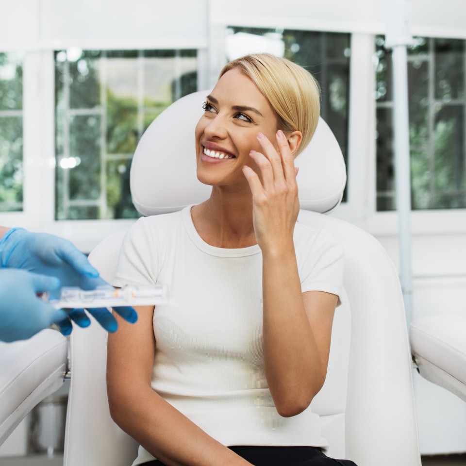 Beautiful and happy blonde woman at beauty medical clinic. She is sitting and talking with female doctor about face esthetics treatment.