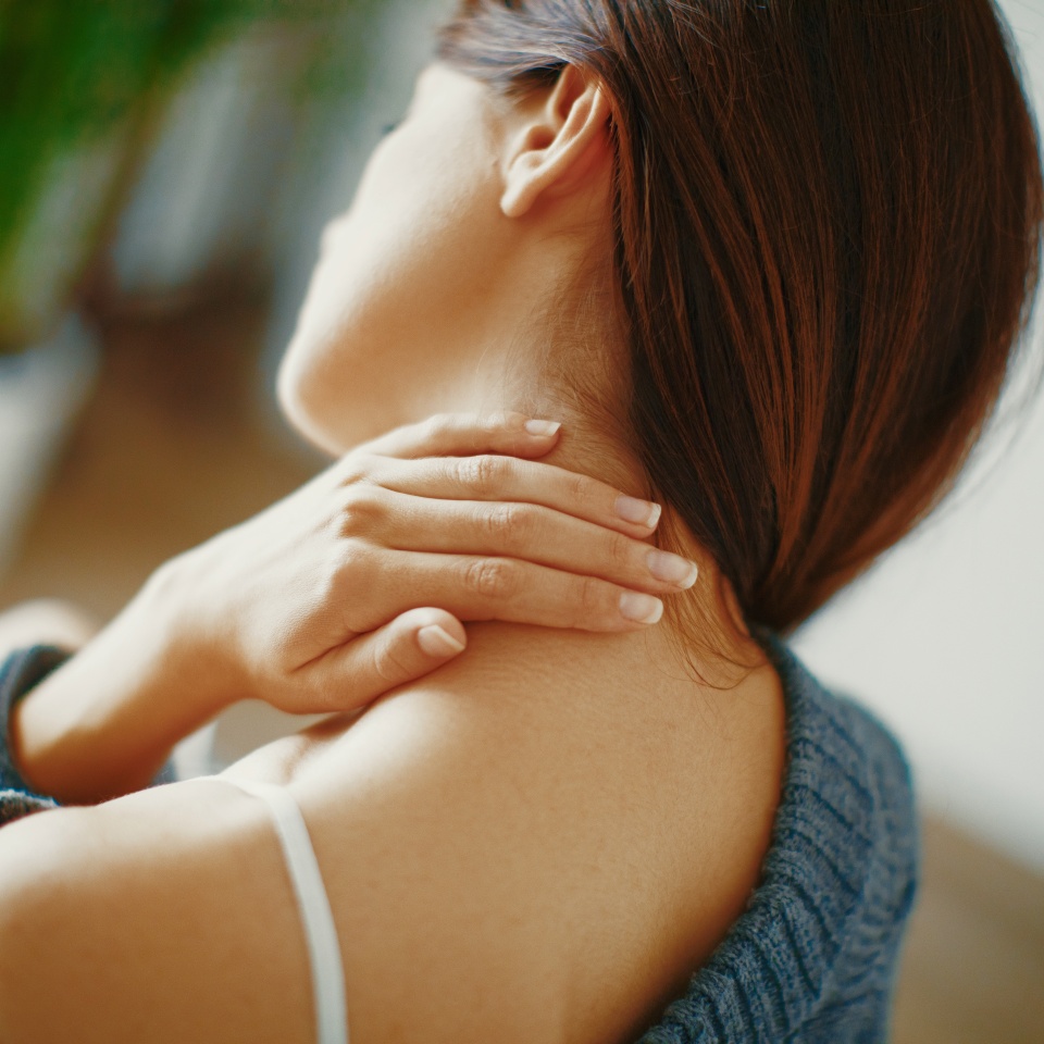 Close up of a brunette woman massaging her neck in a bedroom