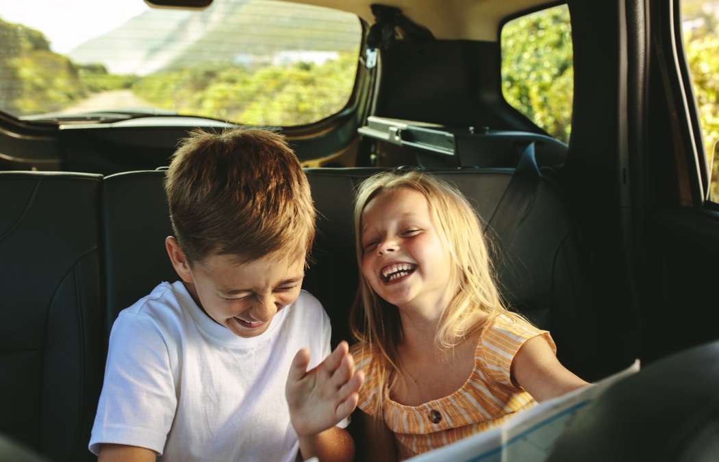 Siblings sitting on backseat of car looking at map and smiling. Kids traveling in a car on roadtrip playing with a map.