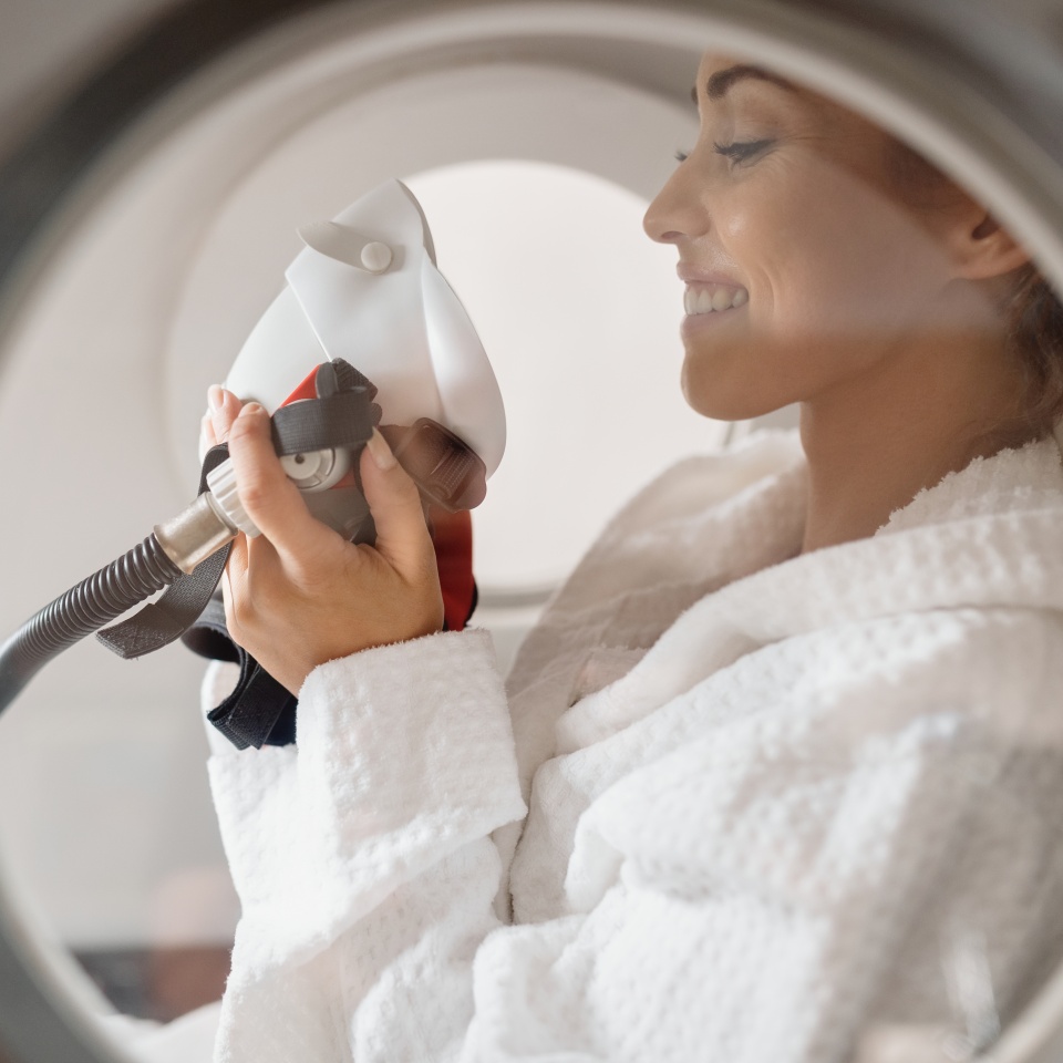 Side view of happy woman receiving oxygen therapy at hyperbaric chamber at health spa.
