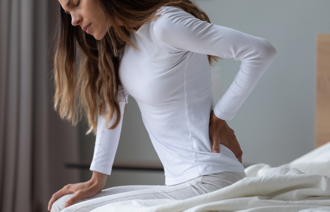 Close up unhappy woman wearing pajama rubbing stiff back muscles after awakening, sitting on bed, upset young female feeling pain, incorrect posture or uncomfortable bed, backache after sleep