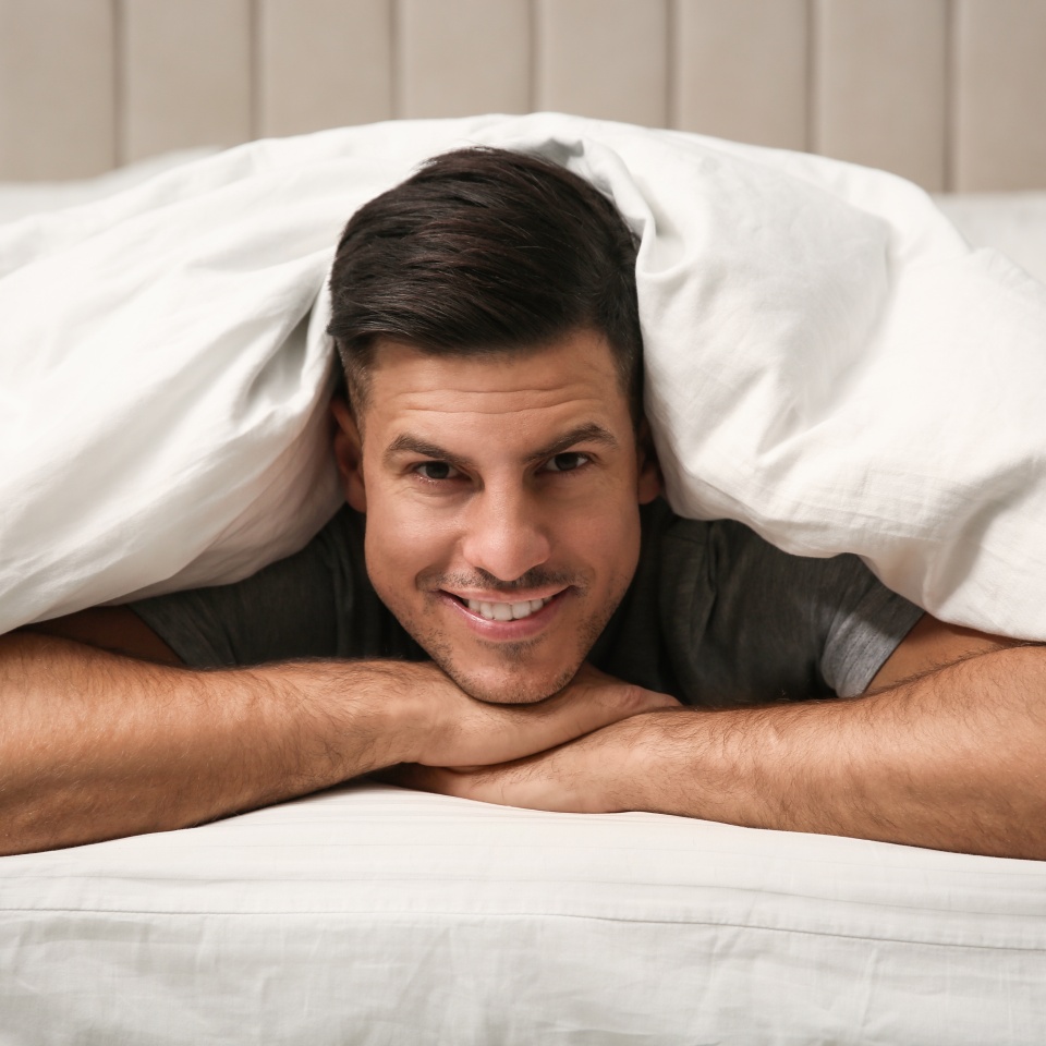 Handsome man relaxing under soft blanket in bed at home