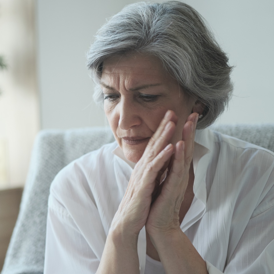 Elderly senior woman massaging her temples to reduce her headache. Older lady feeling scared, anxious, and thinking of sickness or mental health while suffering from a severe migraine or memory loss.