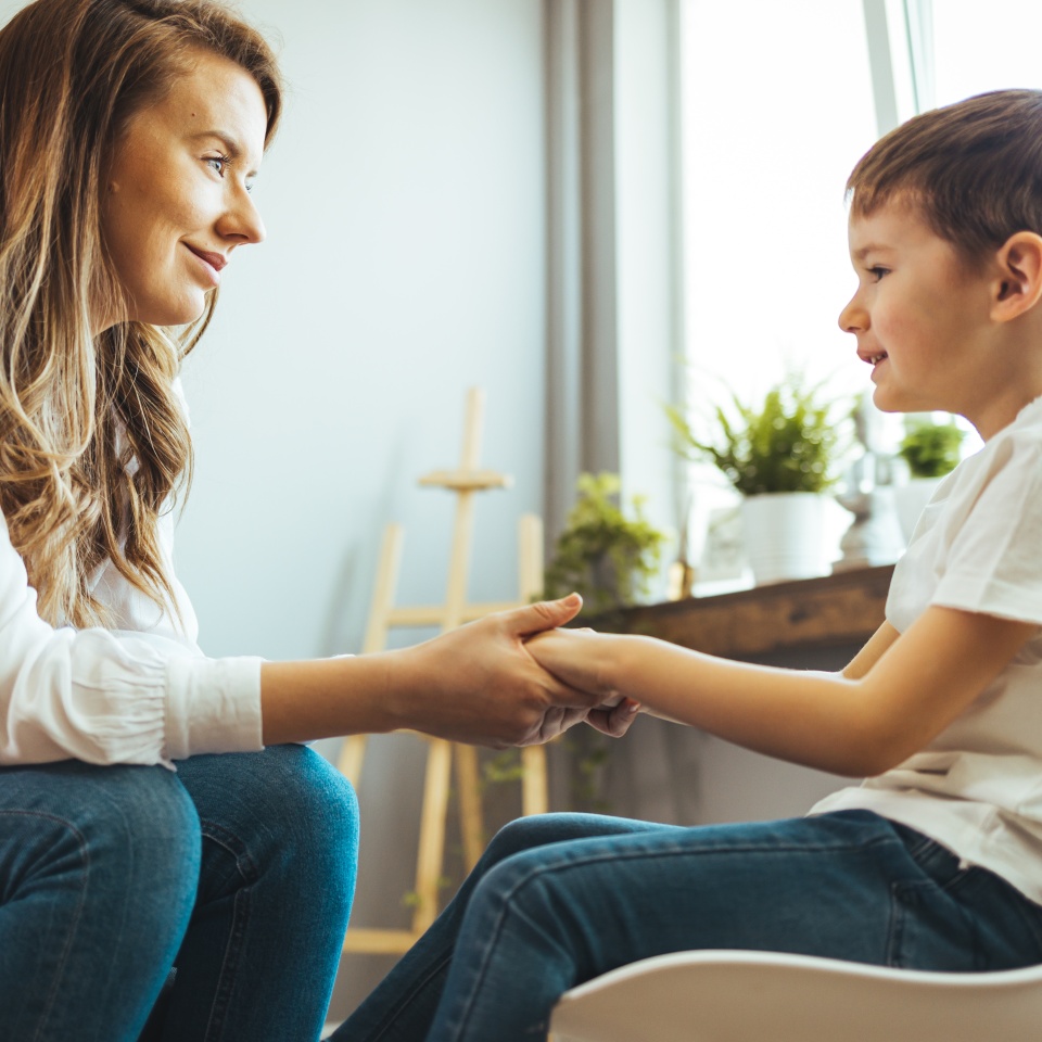 Young boy having therapy with a child psychologist. Smiling woman talking to boy. Friendly young child psychologist talking with little boy suffering from emotional disorder in bright office