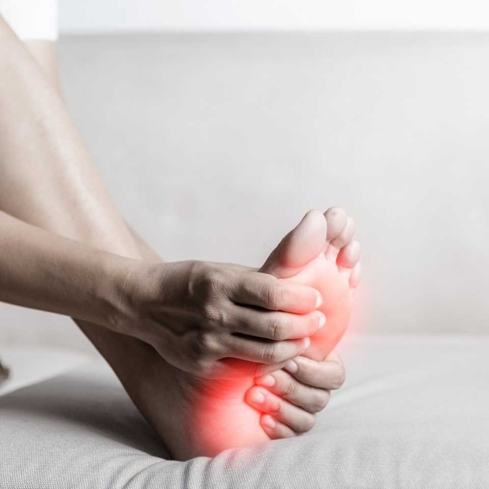 Foot pain, Asian woman sitting on sofa feeling pain in her foot at home, female suffering from feet ache use hand massage relax muscle from soles in home interior, Healthcare and podiatry medical