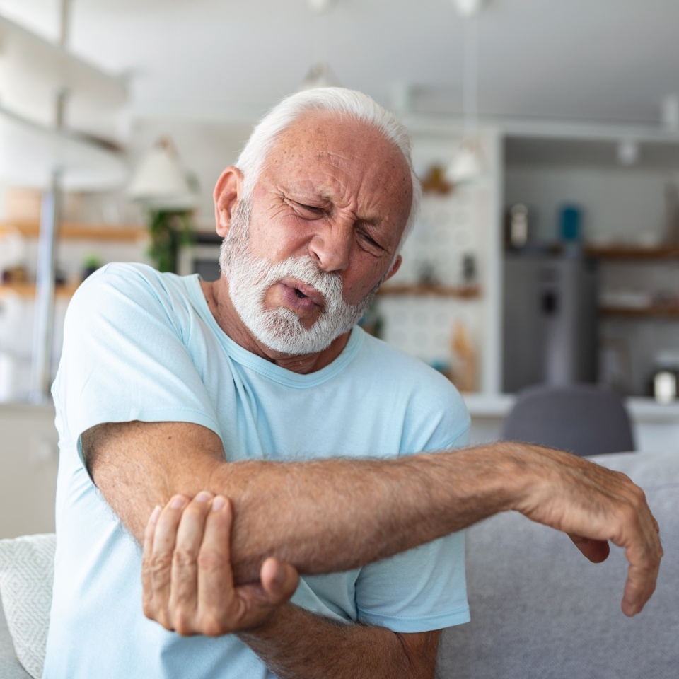 Senior man with arm pain.Old male massaging painful hand indoors. Old man hand holding his elbow suffering from elbow pain. Senior man suffering from pain in hand at home. Old age, health