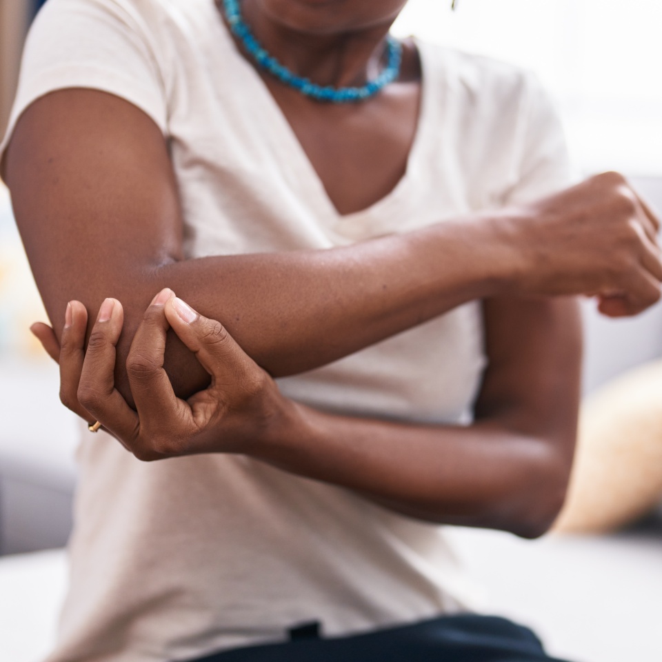 Middle age african american woman sitting on sofa suffering for elbow pain at home