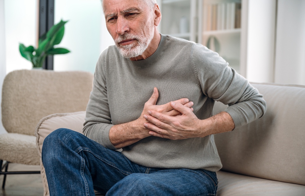 mature man feeling unwell, cardiac pain in chest, sitting on couch at home and need medical help. senior male has heart attack symptom. healthcare and medicare concept