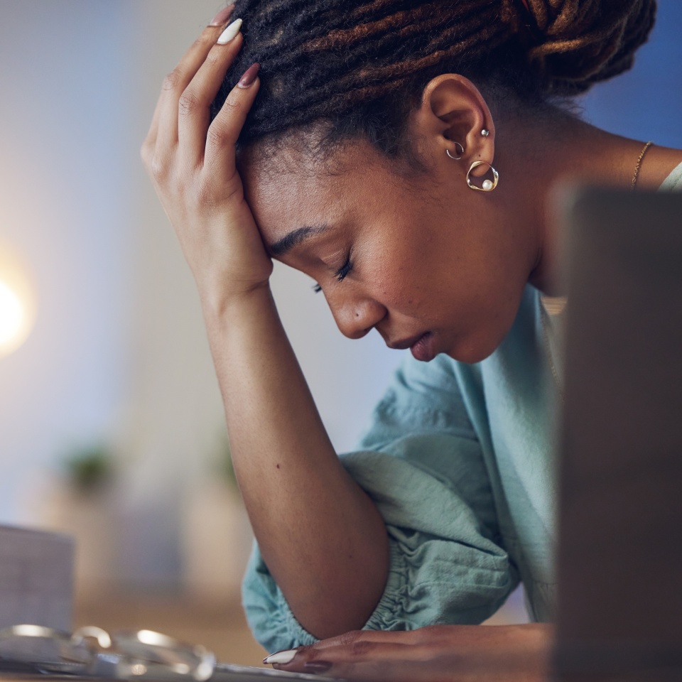 Business woman, depression and stress in an office at night working late on deadline. Tired African entrepreneur person with hands on head for pain, burnout or regret for mistake or fail at work