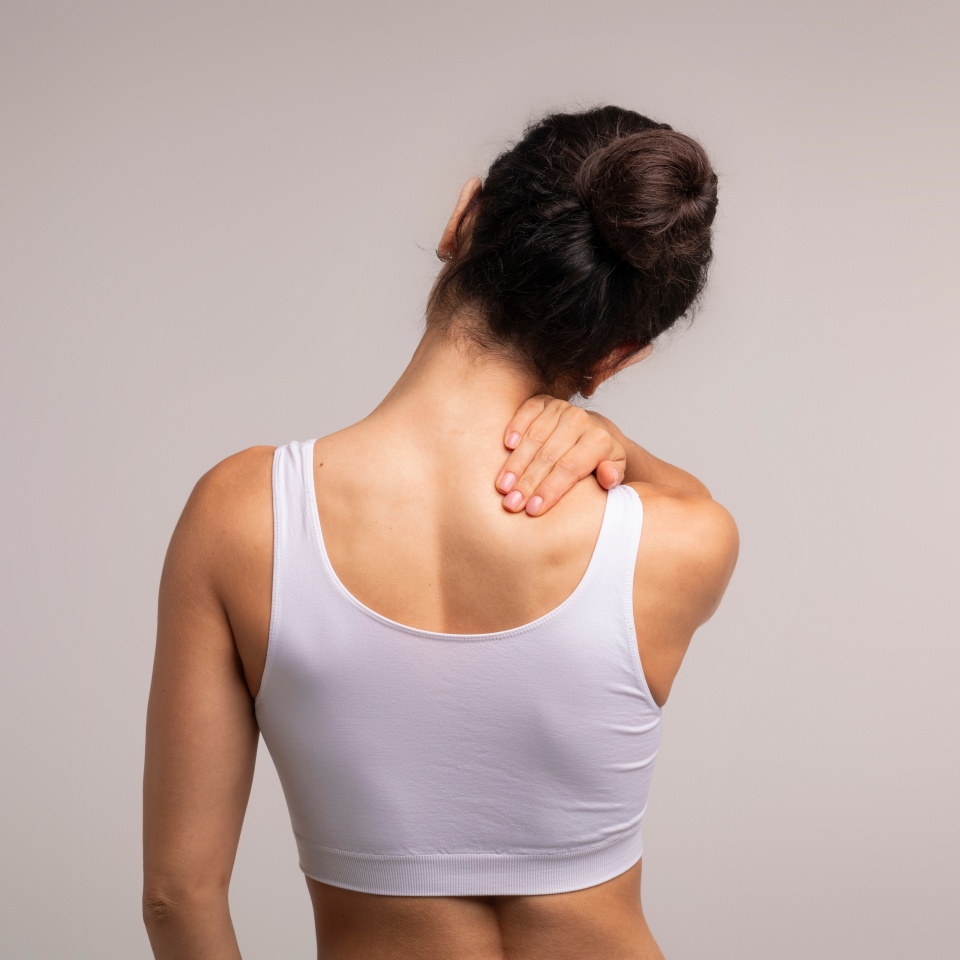 Unrecognizable brunette woman with neck and back pain rubbing her painful body neck area, lady suffering from office syndrome, back view, grey studio background, copy space