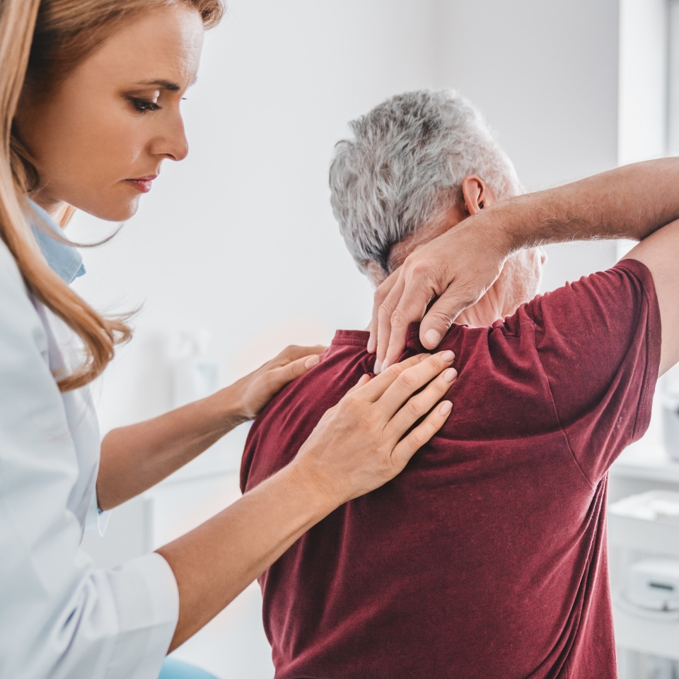 Caucasian female orthopedist examining senior male patient's back in clinic. Spinal injury treatment prevention. Chiropractic concept. Healing process