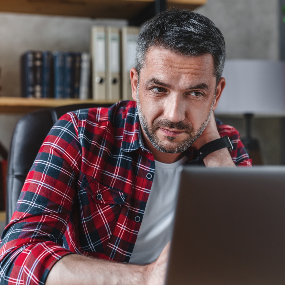 Caucasian man office worker freelancer touching neck due to tiredness from remote work on laptop computer for a long time at his home coworking. Overworking concept