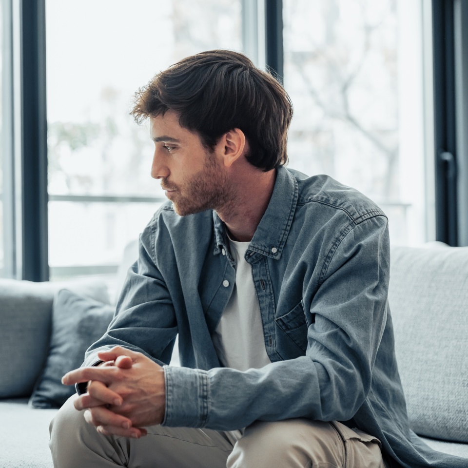 Thoughtful serious man sitting on sofa alone at home, lost in thoughts, thinking about problem solving, feeling lonely, making important decision, having psychological problem, side view