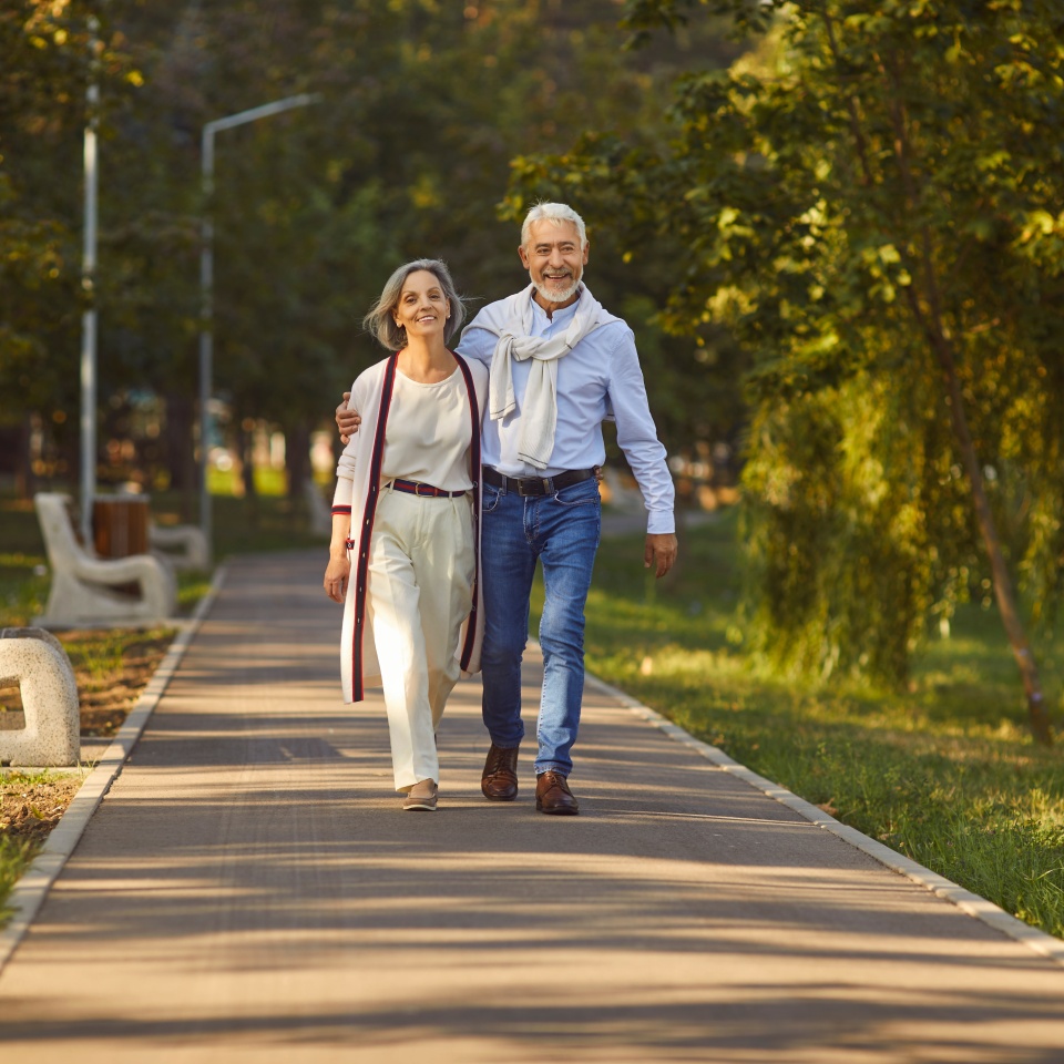 Happy smiling senior couple family hugging while walking in summer city park enjoying retirement and spending time together in nature. Romance, love. care and elderly people relationship concept.