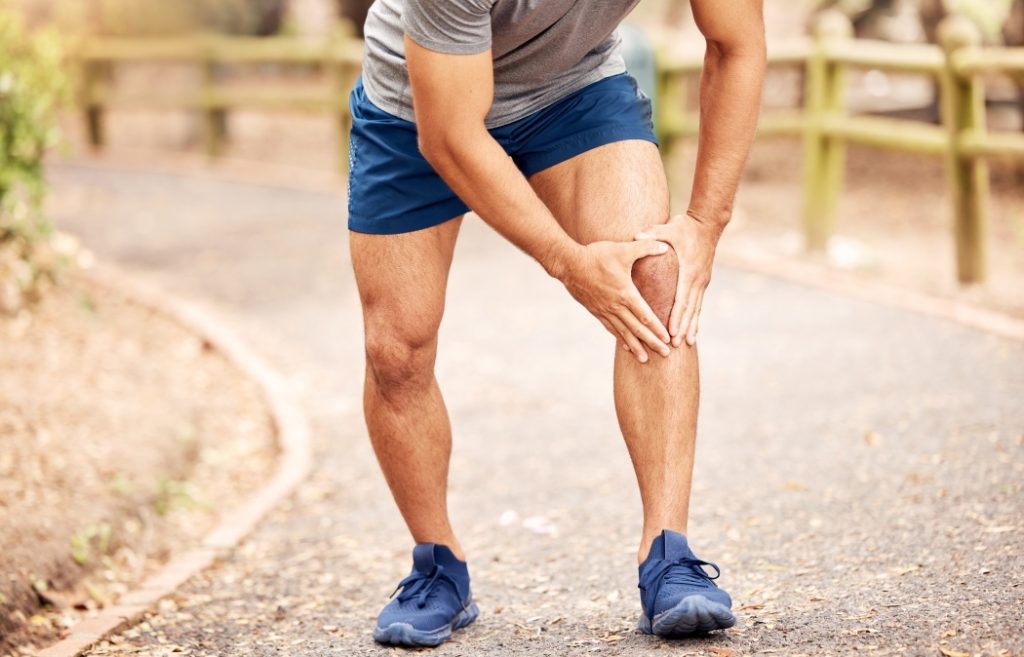 Outdoor, knee pain and hands of person after fitness accident, injury and muscle tension. Nature, road and male runner with fibromyalgia, leg inflammation and massage joint during training session