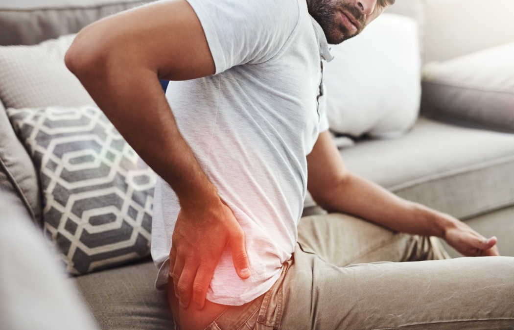 Back pain, hands and man on sofa with inflammation glow, joint or anatomy risk in his home. Red, backache and male person in a living room with muscle, burnout or spine, bone and emergency in house