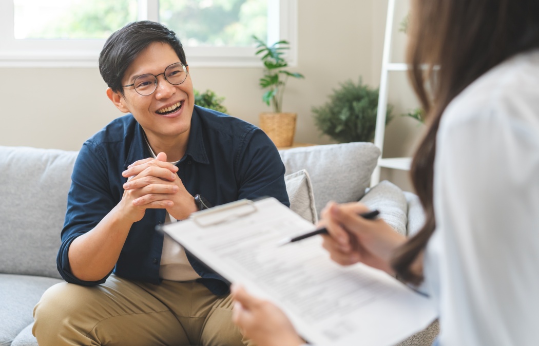Psychology, depression. smile asian young male, man patient mental sitting on couch, explained symptom with psychologist, psychiatrist while doctor woman taking notes at clinic. Encouraging, therapy.