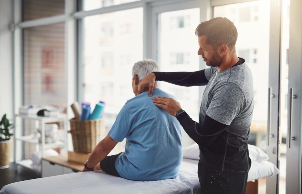 Physiotherapy, shoulder pain and person with senior man for medical care, consulting and wellness. Chiropractor, healthcare and physical therapist and client for rehabilitation, massage or assessment