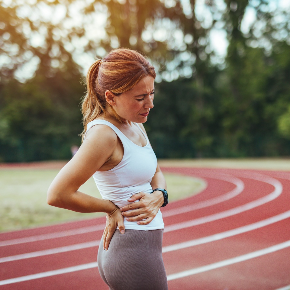 Tired Young Sport girl feel pain on her back and hip while exercising, health care concept. Back pain - woman having painful muscle injury in lower back.