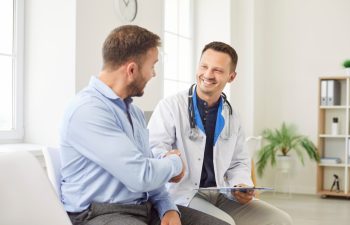 Doctor or nurse shakes hands with a male patient during visit to the hospital clinic. The handshake symbolizes professional medical care, trust, and the importance of patients healthcare.