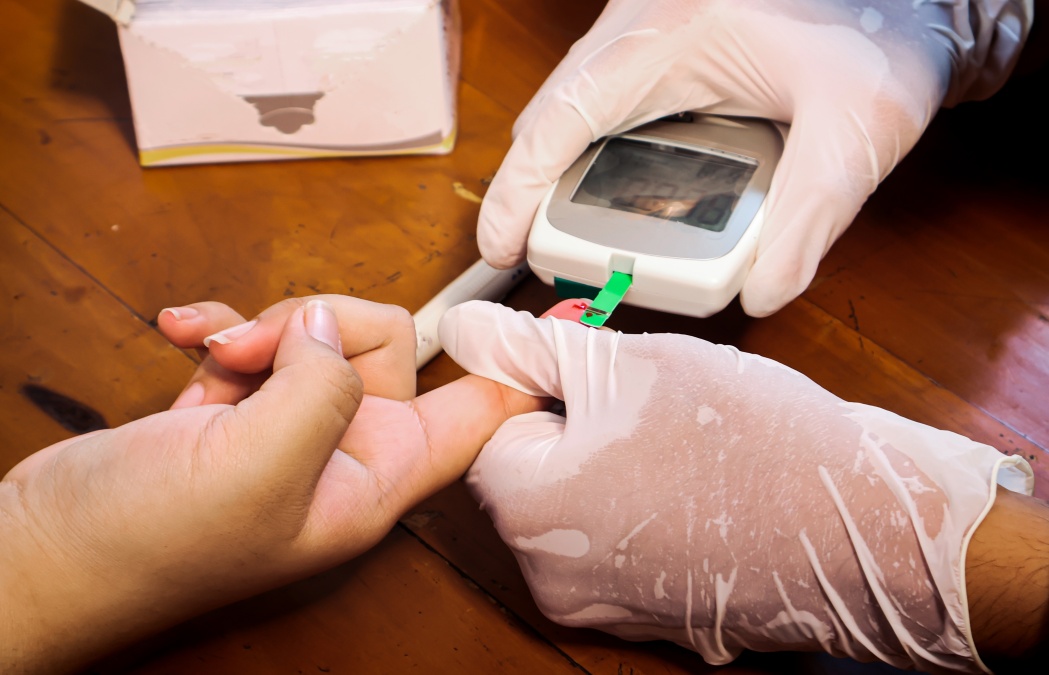 Close-up of a doctor wearing gloves, using a glucometer to measure a patient's blood glucose levels during a routine medical checkup. Focus on medical device, hygiene, and diabetes screening