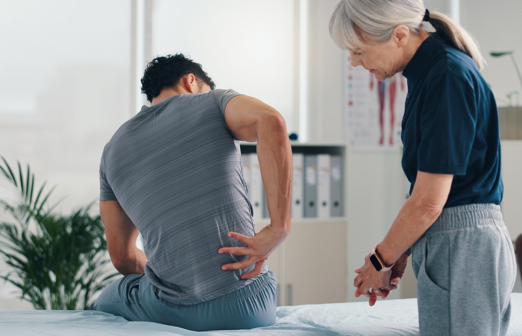 Back pain, physical therapy and patient at consultation for problem, inflammation or muscle strain. People, chiropractor and treatment for injury, rehabilitation and recovery of spinal ligaments