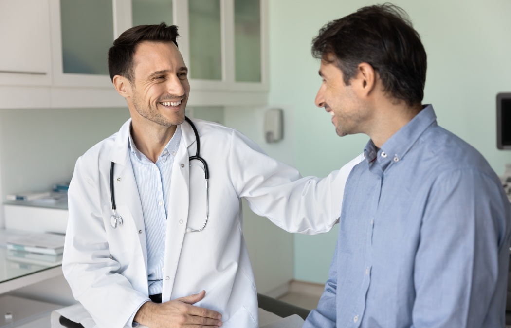 Cheerful supportive empathetic doctor man touching shoulder of patient on appointment in hospital office, congratulating on successful treatment result, rehabilitation, good checkup