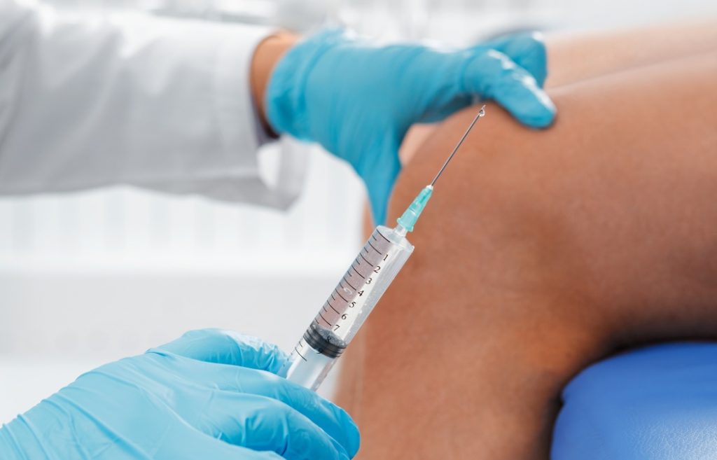 Close-up of doctor preparing syringe for knee injection. Medical treatment and healthcare concept.