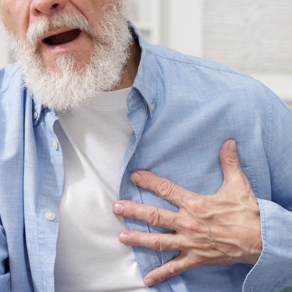 Heart attack. Senior man suffering from pain in chest on sofa at home, closeup