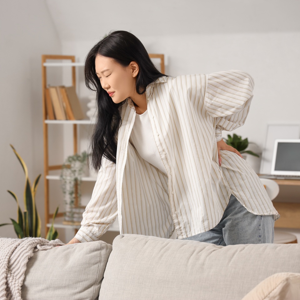 Beautiful young Asian woman suffering from back pain at home