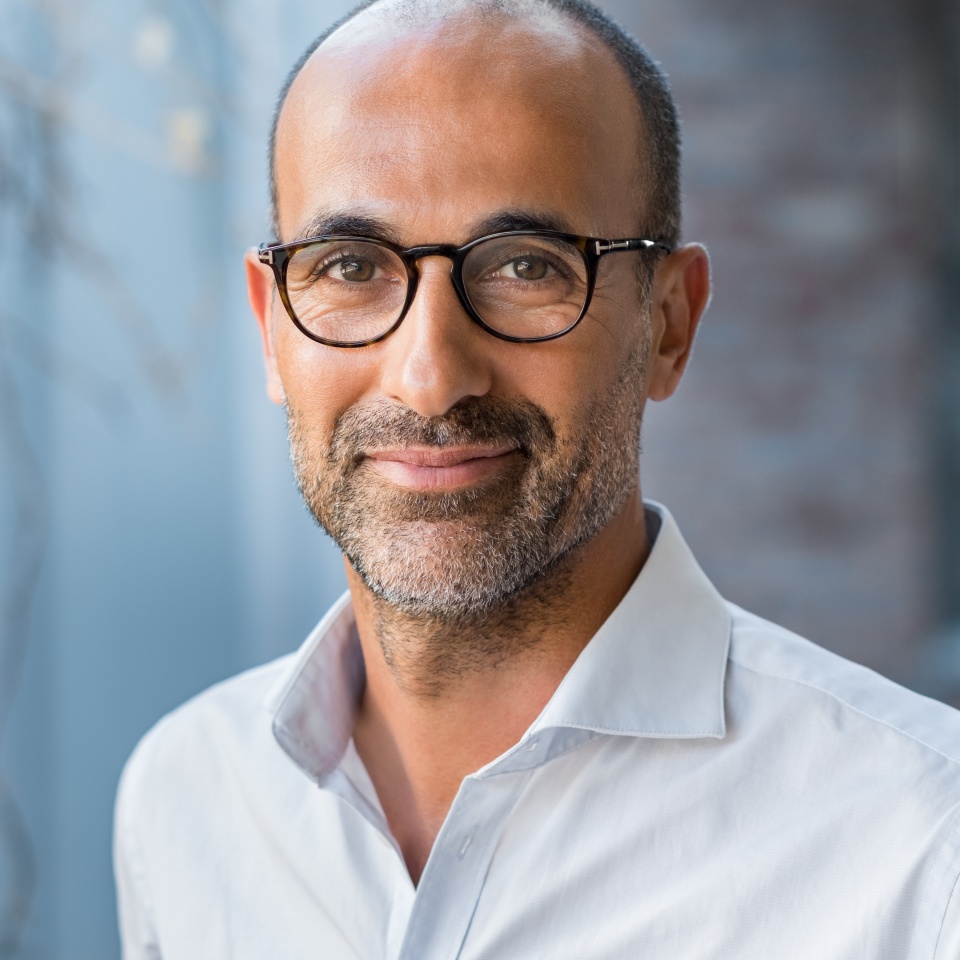 Portrait of happy mature man wearing spectacles and looking at camera outdoor. Man with beard and glasses feeling confident. Close up face of hispanic business man smiling.