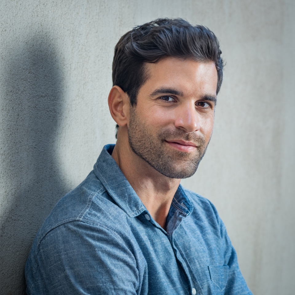 Handsome young man posing on grey background. Portrait of satisfied businessman against grey wall. Close up face of fashionable latin man on grey background.