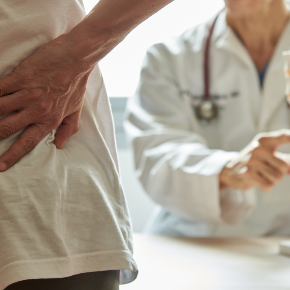 A male doctor explaining lumbar anatomy to female patient complaining of back pain at medical clinic