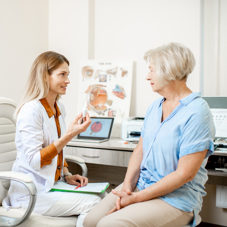 Senior woman patient talking with female ophthalmologist during a medical consultation at the ophthalmologic office. Doctor offering eye medcine for a patient