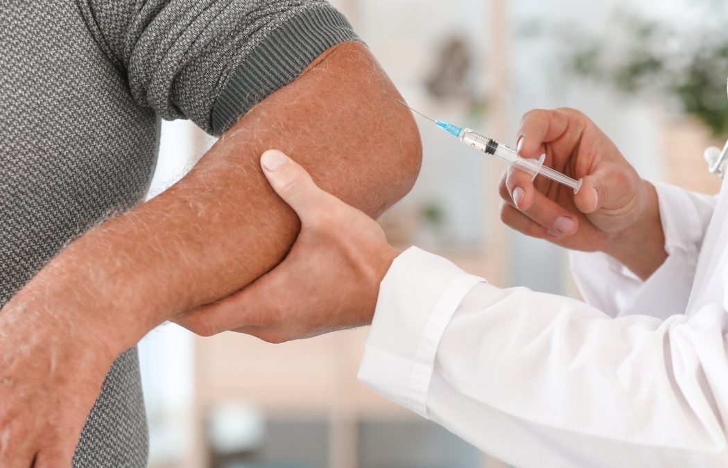 Doctor giving mature man with joint pain injection at home, closeup