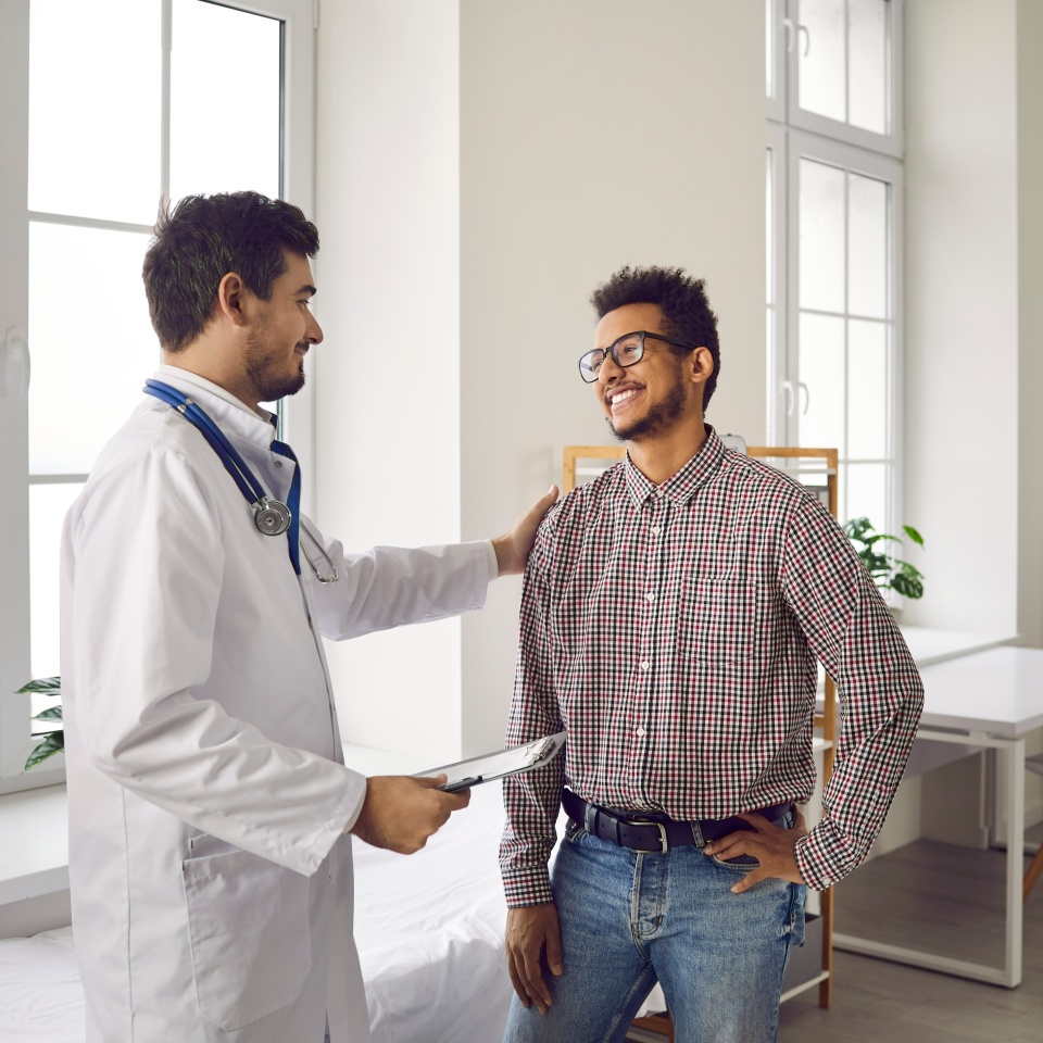 Happy, smiling young man talking to his doctor. Qualified specialist at a modern clinic, hospital or medical center reassuring his male patient after a consultation and health checkup