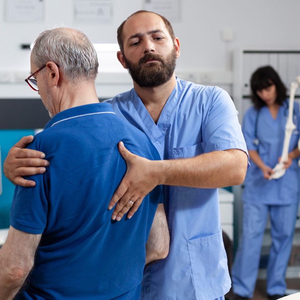 Orthopedic nurse stretching spinal cord and shoulder of elder patient with injury for physiotherapy. Chiropractor giving help to senior man with back pain for physical recovery.