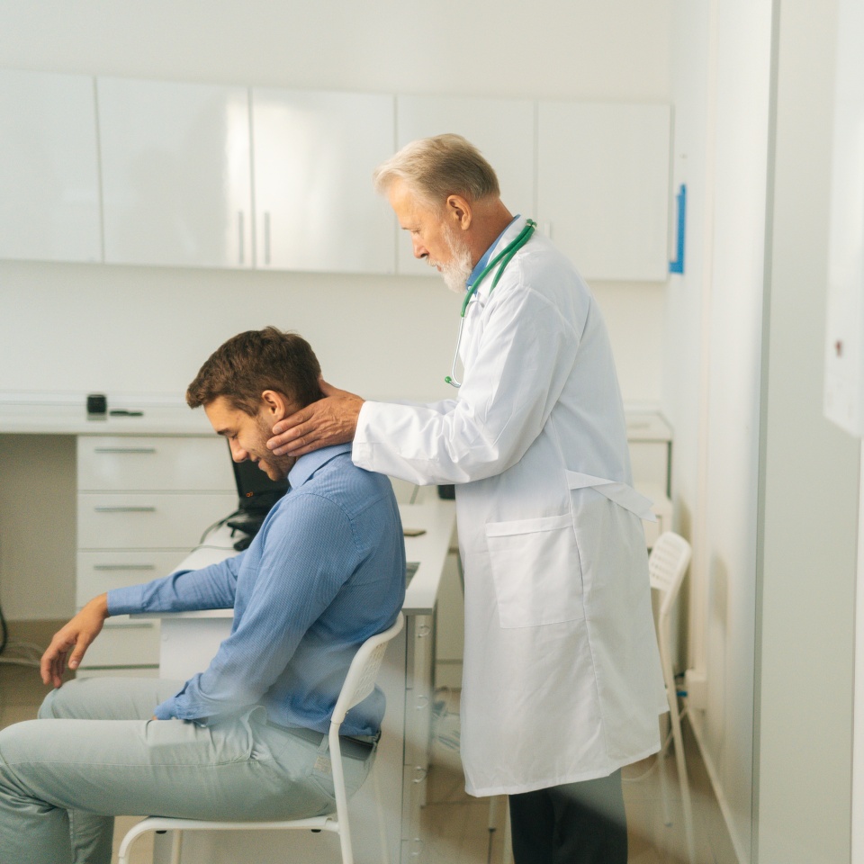 Side view of mature adult male manual therapist turning and bending head of male patient to check his injured neck. Young man on preventive examination of doctor chiropractor on neck diagnostic.