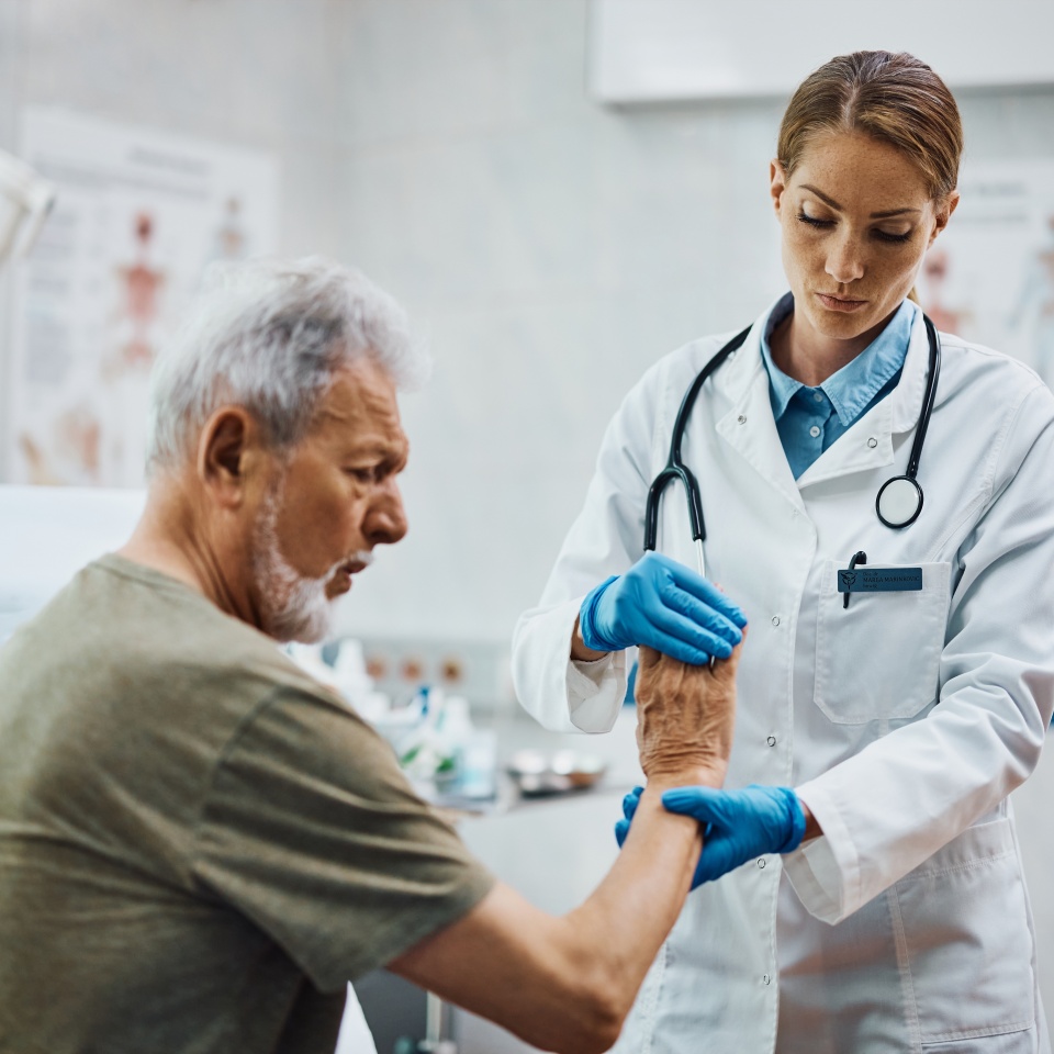 Female physical therapists checking senior patient's hand at medical clinic.