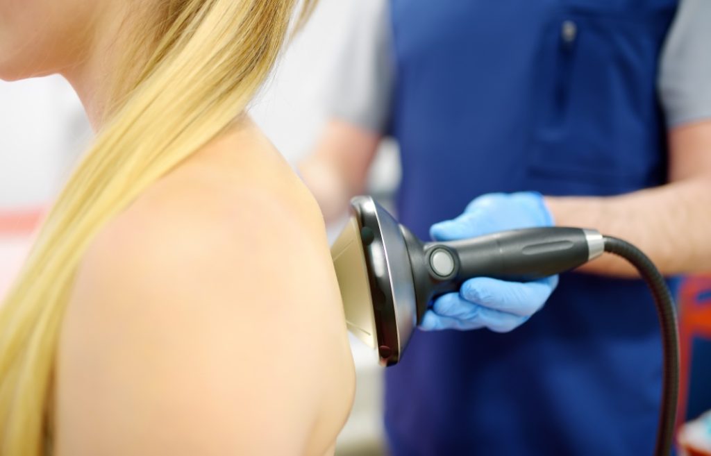 Close up of extracorporeal shockwave therapy in beauty salon. Physical therapy for neck and back muscles with shock waves. Rehabilitation after injury. Modern medical technology.