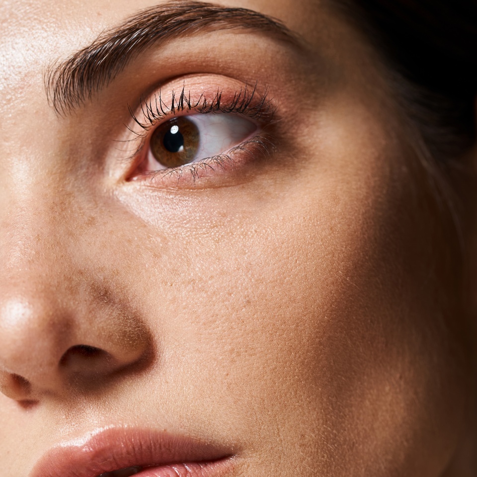 A young caucasian woman with clean skin is featured in a close-up, highlighting her captivating brown eyes.