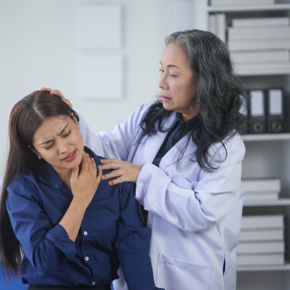 Doctor examining a patient's neck pain in a medical office. The patient appears to be in discomfort while receiving professional care.