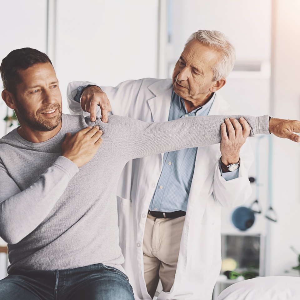 Doctor, man and patient with stretching for shoulder pain with physical therapy, examination or body recovery. Orthopedic, physician or medical expert for arm rehabilitation with healthcare or advice