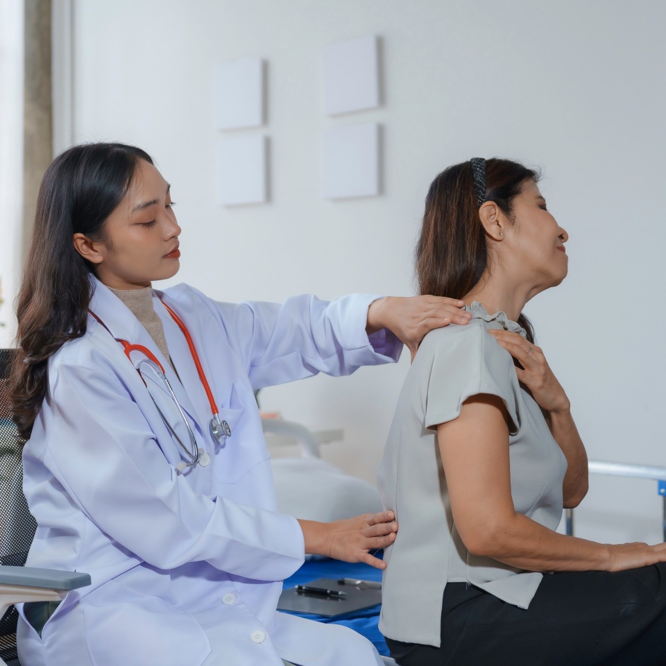 In a hospital room, a senior patient winces in pain as a female doctor examines their shoulder, indicating the need for a medical consultation