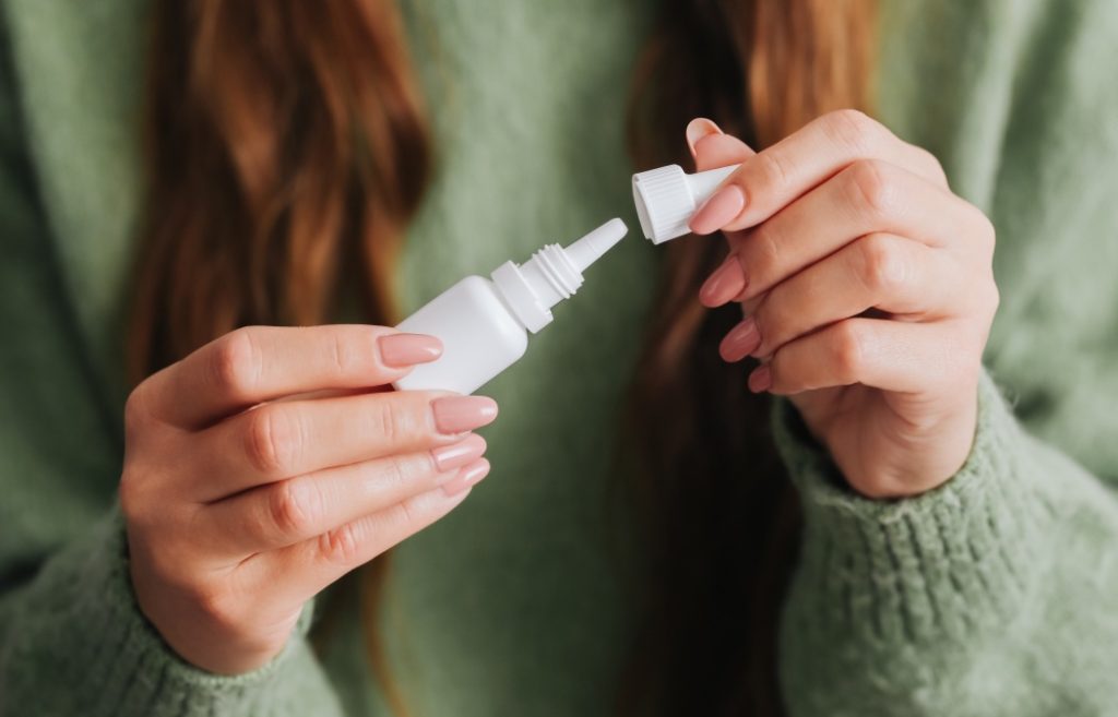 Woman holding a small medicine bottle with liquid eyes or ears drops. Close-up of medical container. Unscrewing bottle cap. Opening alergy fluid medicine. Liquid antibiotics. Health care product.